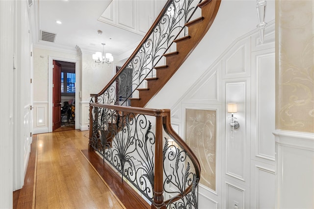 stairs featuring wood-type flooring, a high ceiling, ornamental molding, and a notable chandelier