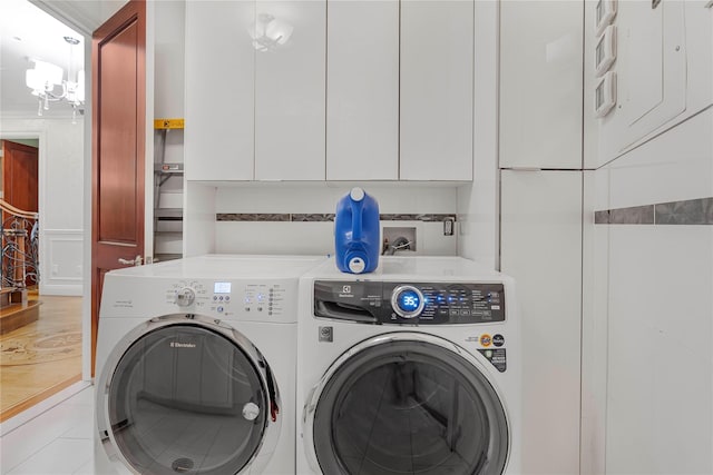 washroom with cabinets, light tile patterned flooring, an inviting chandelier, and washing machine and clothes dryer