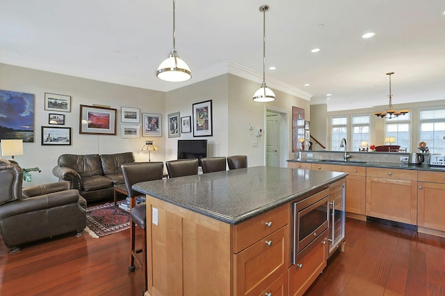 kitchen featuring a breakfast bar, stainless steel microwave, sink, hanging light fixtures, and a kitchen island