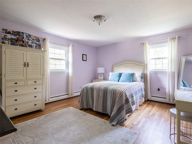 bedroom with multiple windows, a baseboard radiator, and light wood-type flooring