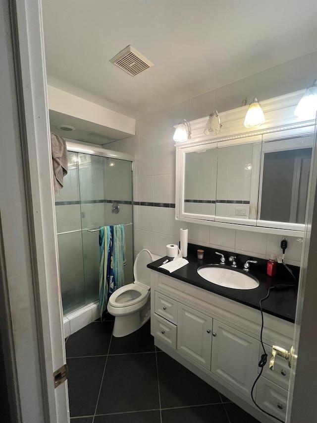 bathroom with tile patterned floors, toilet, a shower with door, vanity, and tile walls