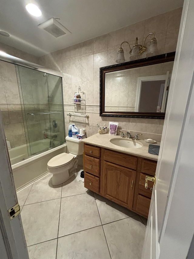 full bathroom with vanity, shower / bath combination with glass door, tile patterned floors, toilet, and tile walls