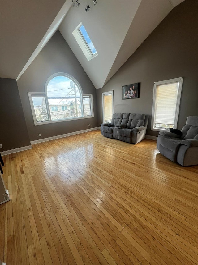 unfurnished living room with high vaulted ceiling, a skylight, and light hardwood / wood-style floors