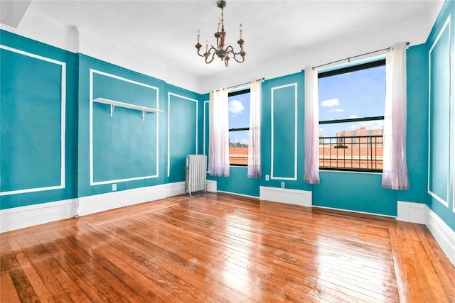 spare room with hardwood / wood-style flooring, radiator, and a chandelier