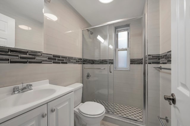 bathroom featuring vanity, toilet, tile walls, and a shower with shower door