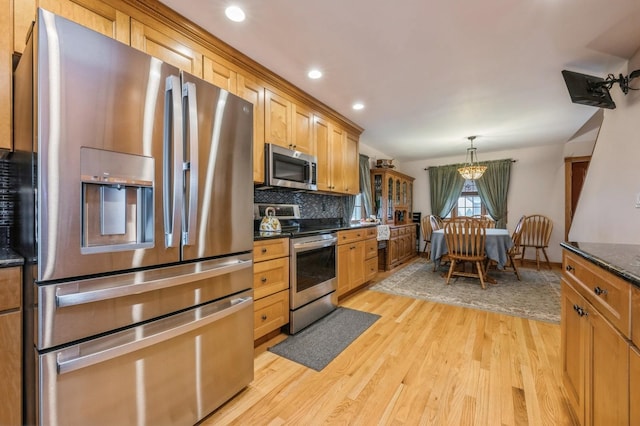 kitchen featuring backsplash, hanging light fixtures, light hardwood / wood-style flooring, dark stone countertops, and appliances with stainless steel finishes