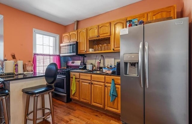 kitchen featuring a kitchen breakfast bar, sink, appliances with stainless steel finishes, and light hardwood / wood-style flooring