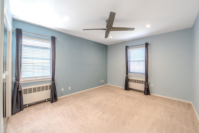 carpeted spare room with ceiling fan, radiator heating unit, and plenty of natural light