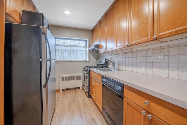 kitchen featuring light wood-type flooring, tasteful backsplash, radiator, sink, and black appliances