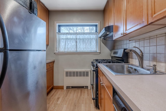 kitchen featuring appliances with stainless steel finishes, backsplash, radiator, sink, and light hardwood / wood-style floors