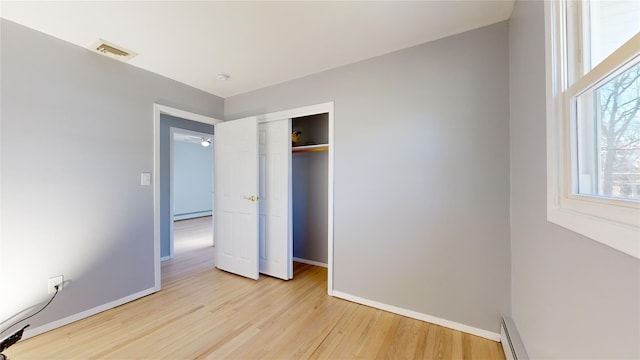 unfurnished bedroom featuring light hardwood / wood-style flooring, baseboard heating, and a closet