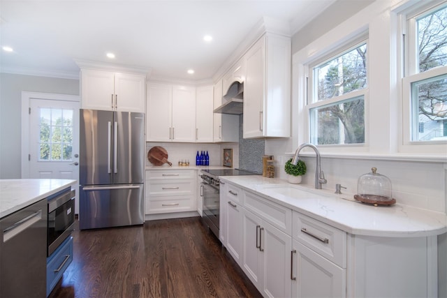 kitchen with backsplash, wall chimney range hood, appliances with stainless steel finishes, light stone counters, and white cabinetry