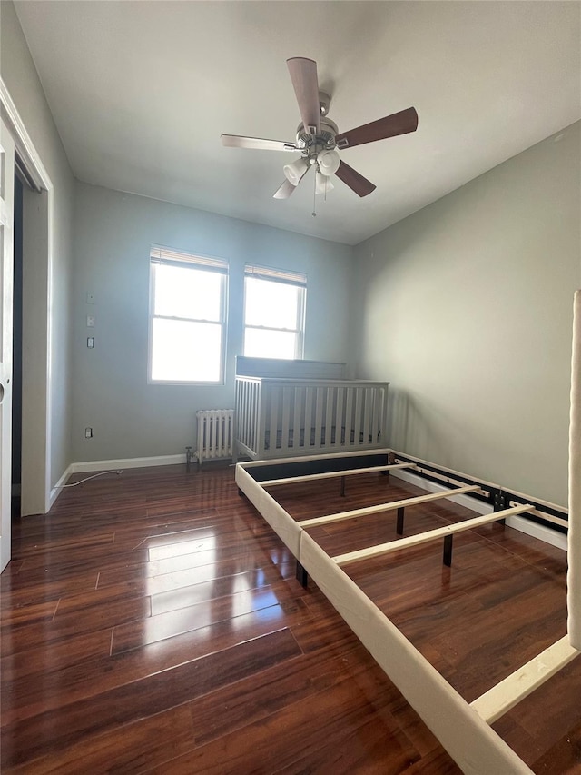 unfurnished bedroom featuring radiator heating unit, dark hardwood / wood-style flooring, and ceiling fan