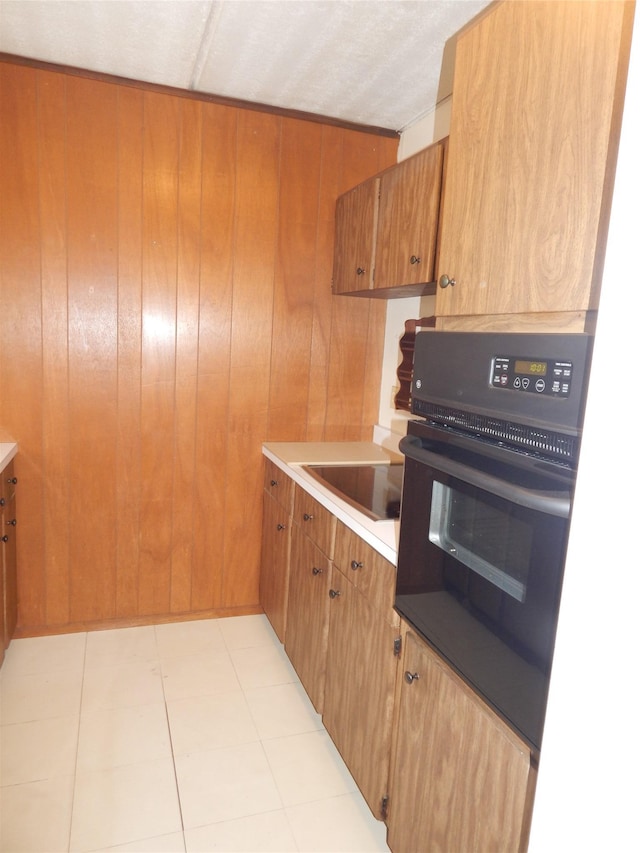 kitchen featuring a textured ceiling, sink, light tile patterned floors, oven, and wood walls