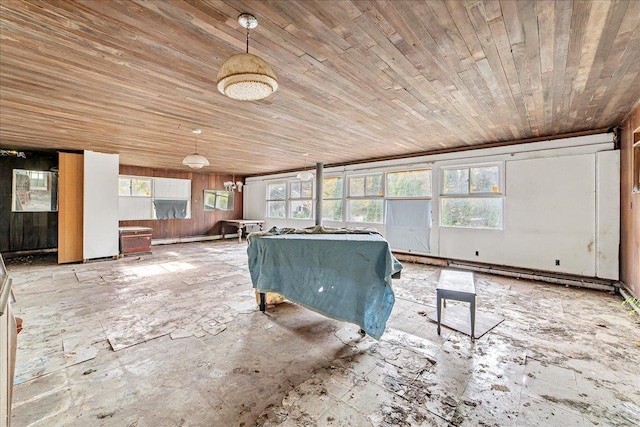 unfurnished living room with a healthy amount of sunlight, a baseboard heating unit, wooden ceiling, and wood walls