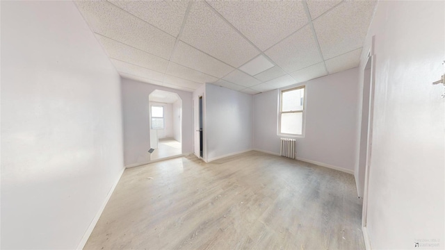 spare room featuring radiator, a drop ceiling, a healthy amount of sunlight, and light hardwood / wood-style flooring