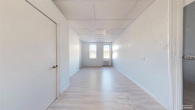 corridor with radiator, a drop ceiling, and light wood-type flooring