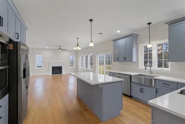 kitchen featuring ceiling fan, a center island, stainless steel appliances, pendant lighting, and gray cabinets