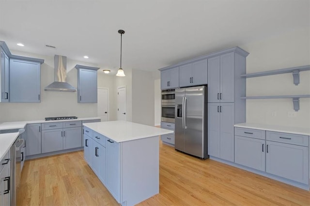 kitchen with a center island, wall chimney range hood, hanging light fixtures, light hardwood / wood-style flooring, and stainless steel appliances