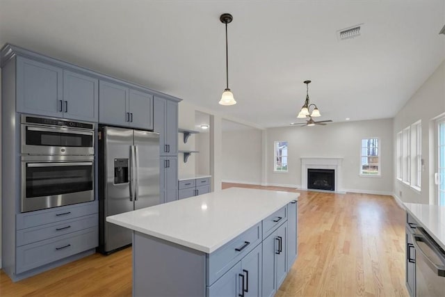 kitchen featuring ceiling fan, a center island, stainless steel appliances, decorative light fixtures, and light wood-type flooring