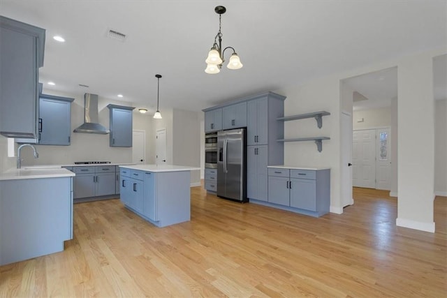 kitchen featuring an inviting chandelier, wall chimney exhaust hood, light hardwood / wood-style floors, a kitchen island, and stainless steel appliances