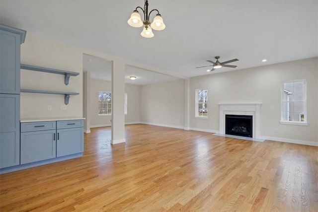 unfurnished living room featuring ceiling fan with notable chandelier and light hardwood / wood-style floors