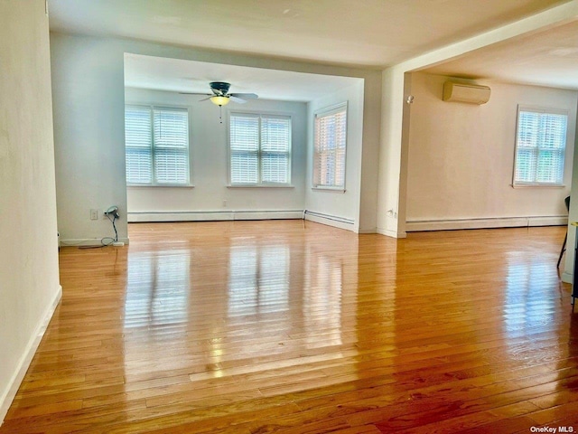 spare room with a wealth of natural light, light hardwood / wood-style floors, baseboard heating, and a wall unit AC