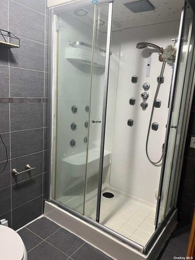 bathroom with tile patterned floors, a shower with shower door, and toilet