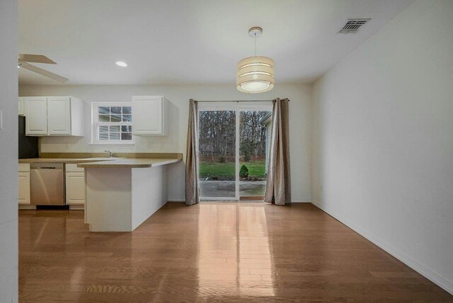 kitchen featuring white cabinets, decorative light fixtures, stainless steel dishwasher, and hardwood / wood-style flooring