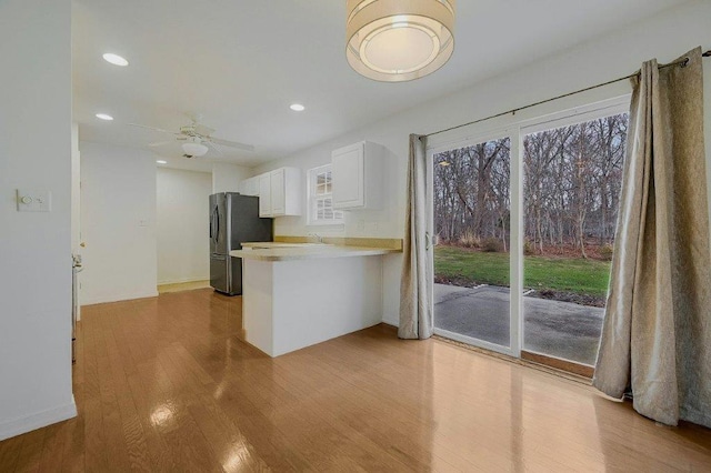 kitchen with white cabinets, light hardwood / wood-style flooring, ceiling fan, stainless steel fridge, and kitchen peninsula