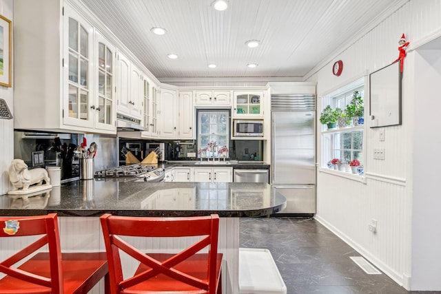 kitchen with kitchen peninsula, a kitchen breakfast bar, built in appliances, and white cabinets