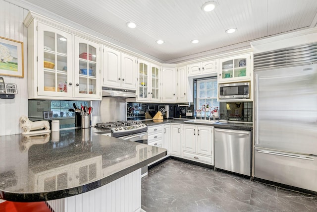 kitchen with kitchen peninsula, backsplash, sink, built in appliances, and white cabinetry