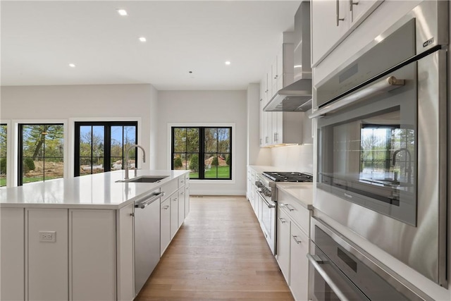 kitchen with a center island with sink, white cabinetry, stainless steel appliances, and wall chimney exhaust hood