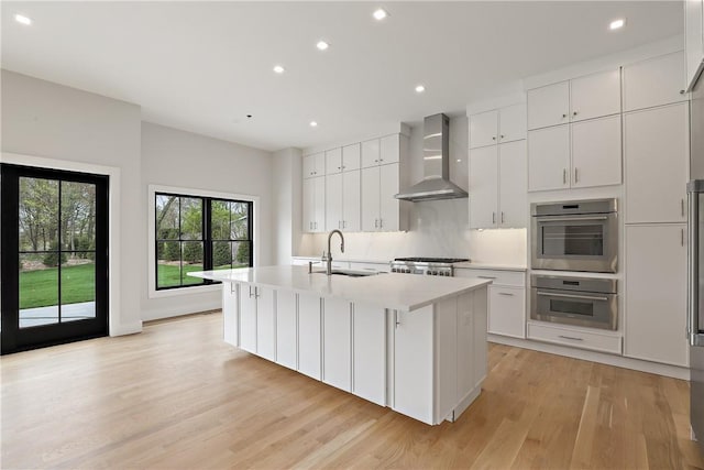 kitchen featuring sink, white cabinetry, wall chimney exhaust hood, and an island with sink