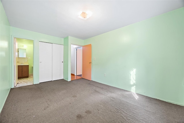 unfurnished bedroom with carpet flooring, a closet, and ensuite bath