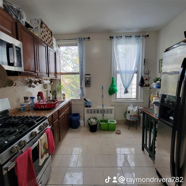 kitchen with backsplash, stainless steel appliances, radiator, and light tile patterned flooring