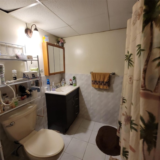 bathroom featuring vanity, a drop ceiling, tile patterned floors, toilet, and tile walls