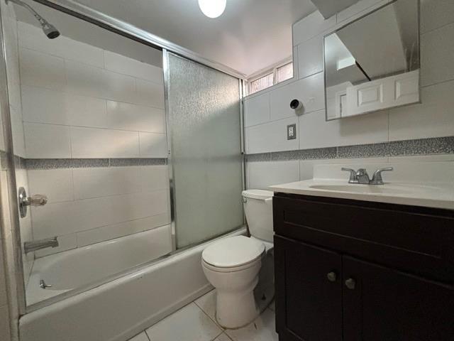 full bathroom with combined bath / shower with glass door, tile patterned floors, toilet, vanity, and tile walls