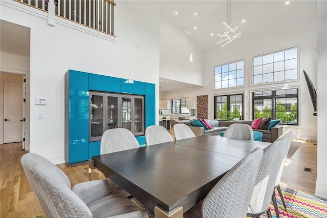 dining space with light hardwood / wood-style floors, a high ceiling, and an inviting chandelier