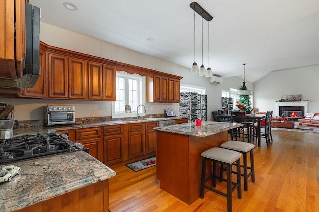 kitchen featuring a kitchen island, light wood-type flooring, hanging light fixtures, and dark stone counters