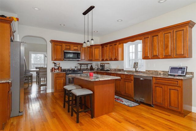 kitchen with a wealth of natural light, a center island, stainless steel appliances, pendant lighting, and light wood-type flooring