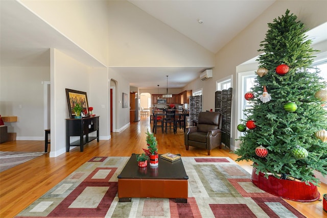 living room with a wall unit AC, high vaulted ceiling, and light wood-type flooring