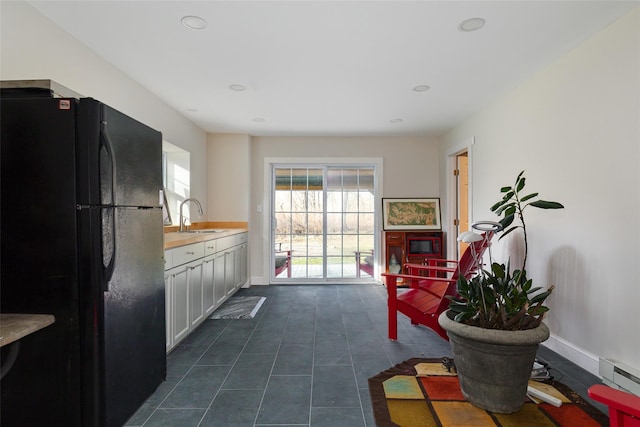 kitchen featuring white cabinetry, black fridge, sink, and baseboard heating