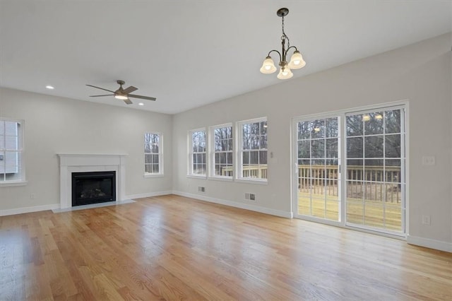 unfurnished living room with ceiling fan with notable chandelier, a healthy amount of sunlight, and light hardwood / wood-style flooring