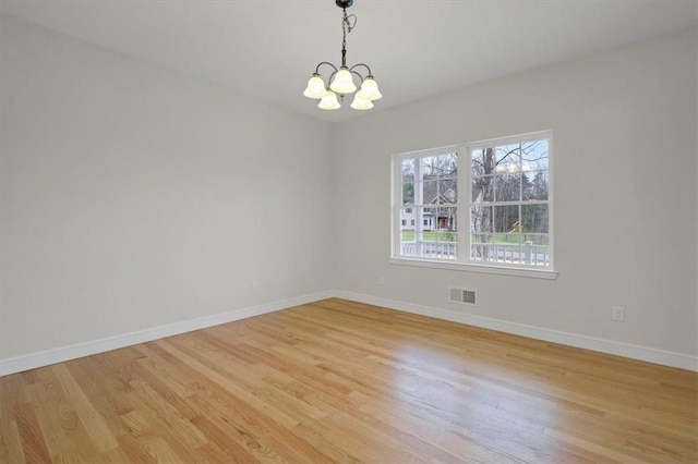 empty room with light wood-type flooring and a chandelier