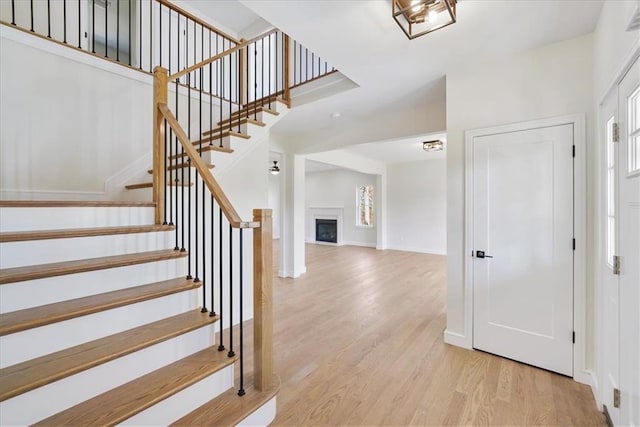 foyer entrance with baseboards, stairway, a fireplace, wood finished floors, and plenty of natural light