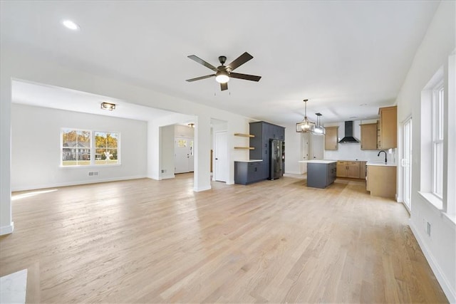 unfurnished living room with visible vents, ceiling fan with notable chandelier, a sink, light wood-style floors, and baseboards