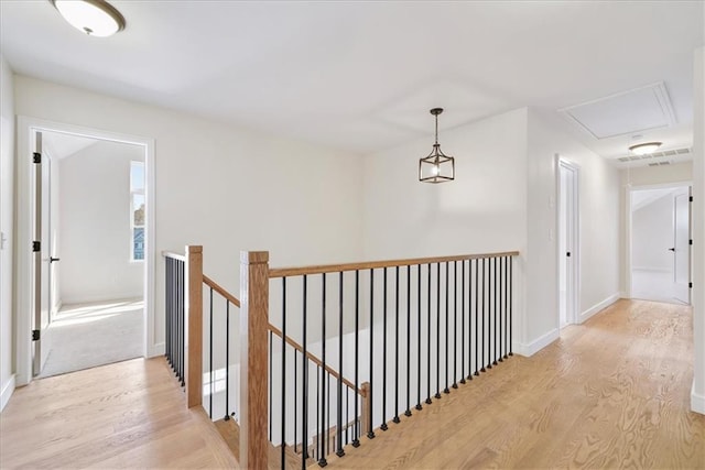 corridor with baseboards, light wood-type flooring, an upstairs landing, and attic access