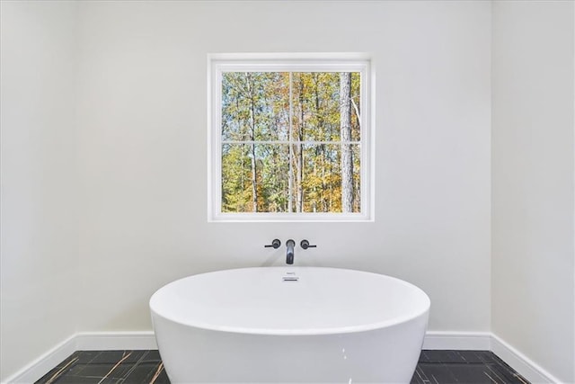 bathroom with tile patterned flooring, a freestanding bath, and baseboards