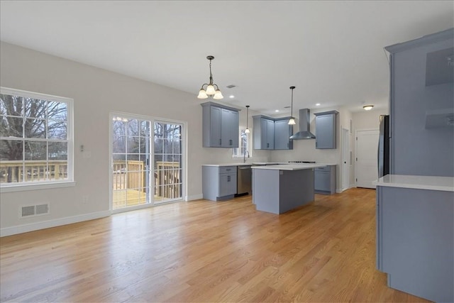 kitchen with light wood-type flooring, stainless steel appliances, wall chimney range hood, pendant lighting, and a center island